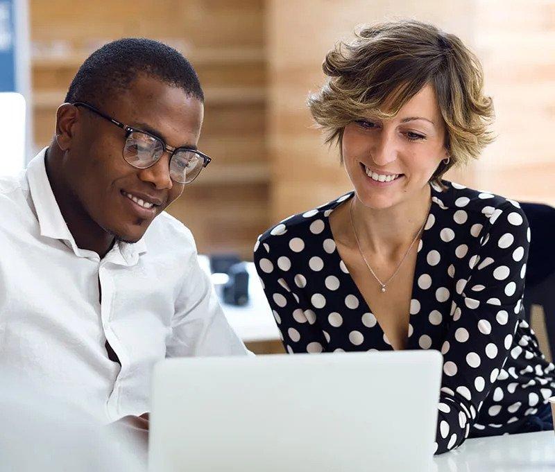 Two employees smiling and staring at a laptop
