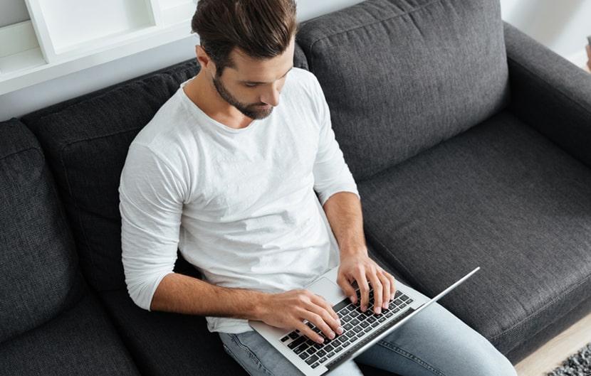 A guy pressing a laptop on a couch